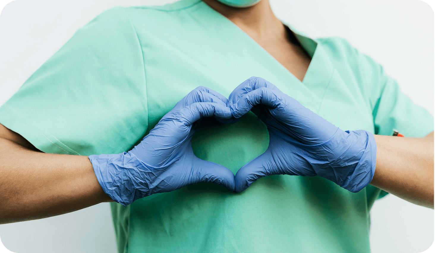 Helsearbeider med munnbind og hansker viser hjerteform med hendene i medisinsk setting.